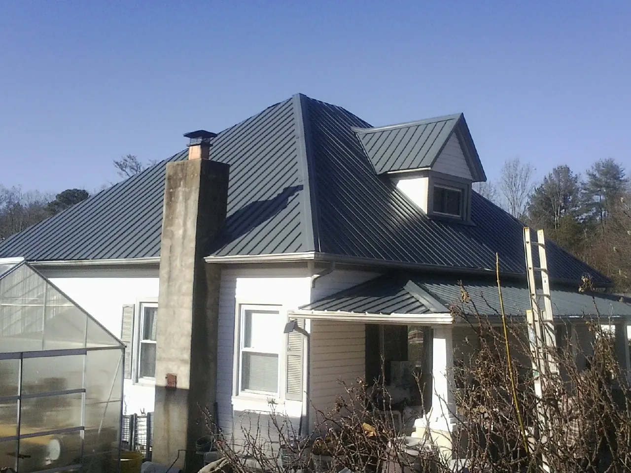 Dark blue standing seam metal roof on a white farmhouse with dormer — Slate & Tile Roof Repair by Roofing Brothers in Sylvan Beach