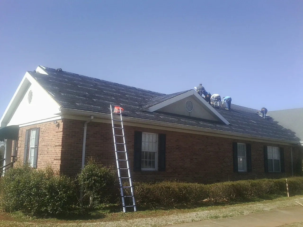 Crew tearing shingles off a brick ranch roof with a ladder set — Metal Roof Repair work by our crew in Sylvan Beach