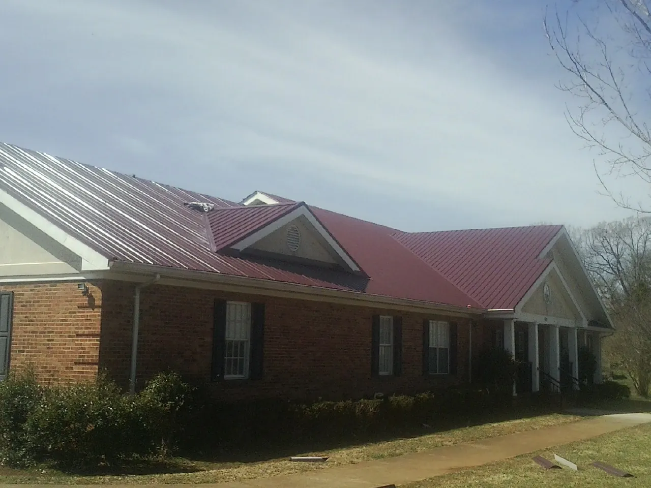 Red metal roof with gabled entries on a long brick building, from a Hail Damage Roof Repair job in Sylvan Beach
