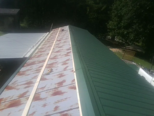 Old rusted panels beside newly installed green metal roofing — Wind Damage Roof Repair by Roofing Brothers in Sylvan Beach