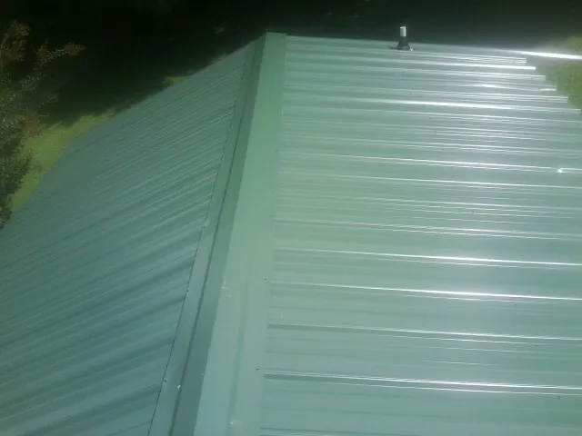 New green metal panels meeting at the ridge of a roof — Flat Roof Repair work by our crew in Sylvan Beach