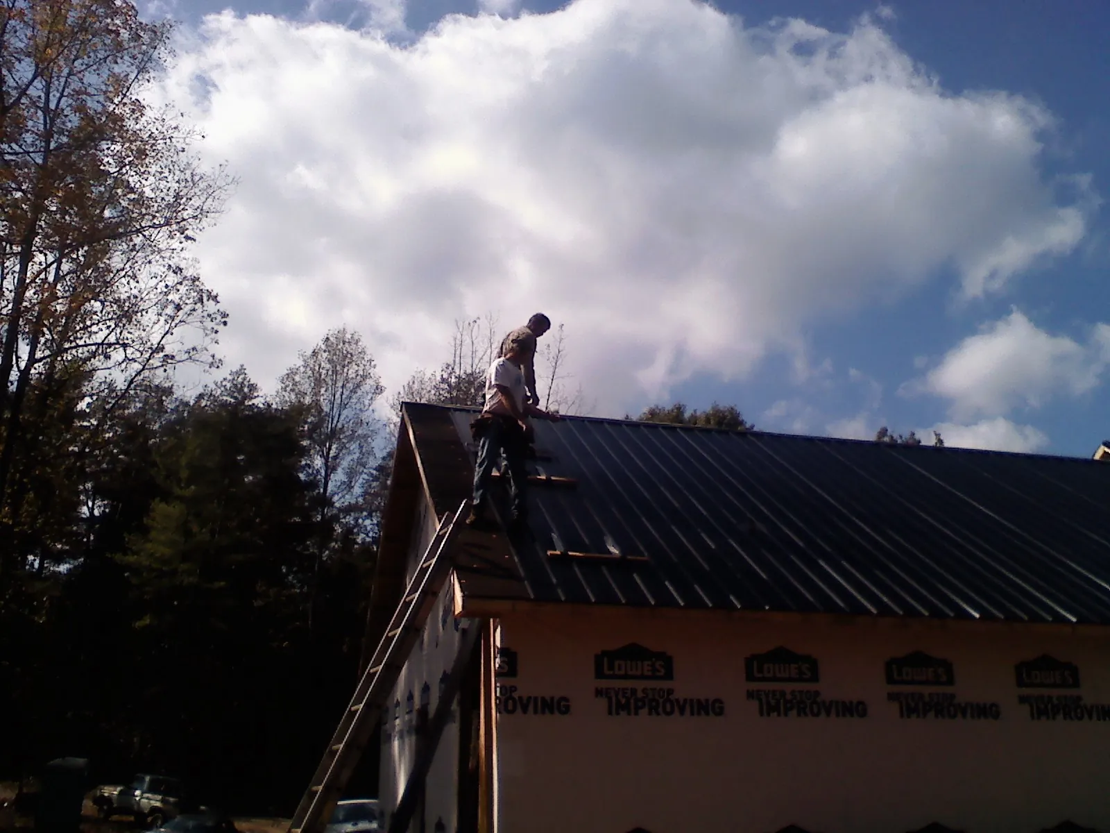 Roofer fastening dark metal panels high against a cloudy sky, from a Roof Inspection job in Sylvan Beach