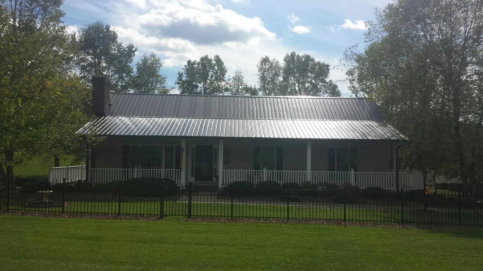 Gray metal roof on a brick ranch with a full width front porch — Gutter Guard Installation work by our crew in Sylvan Beach