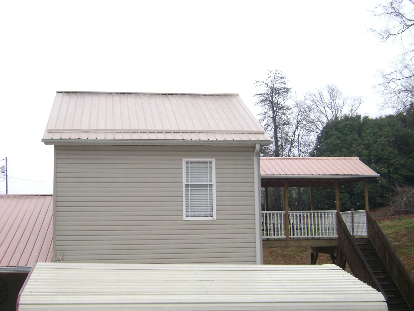 Tan metal roofs on a two story addition and attached porch, from a Roof Replacement job in Sylvan Beach
