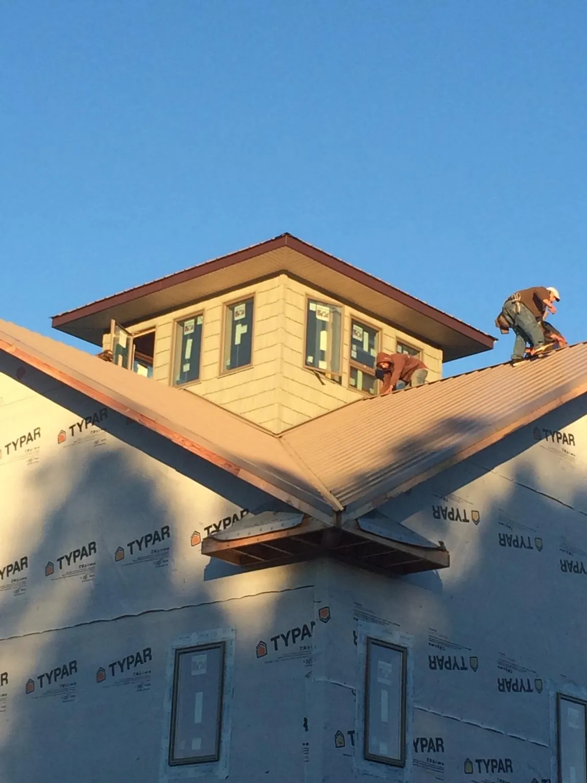 Roofers working around a rooftop cupola on a new metal roof at sunset — Roof Waterproofing in Sylvan Beach by Roofing Brothers
